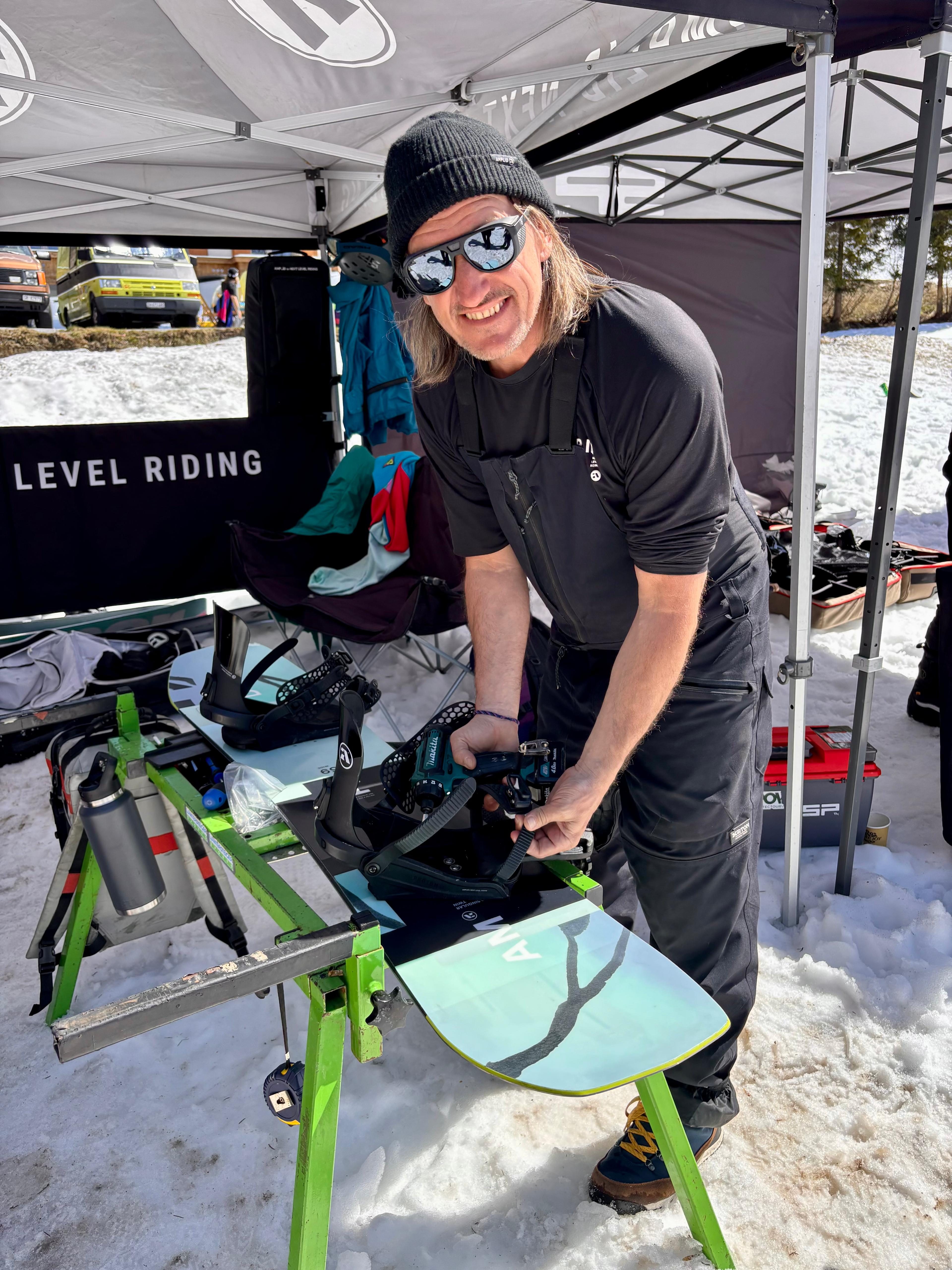 Mann am Snowboard-Tuning-Stand unter Level Riding Banner