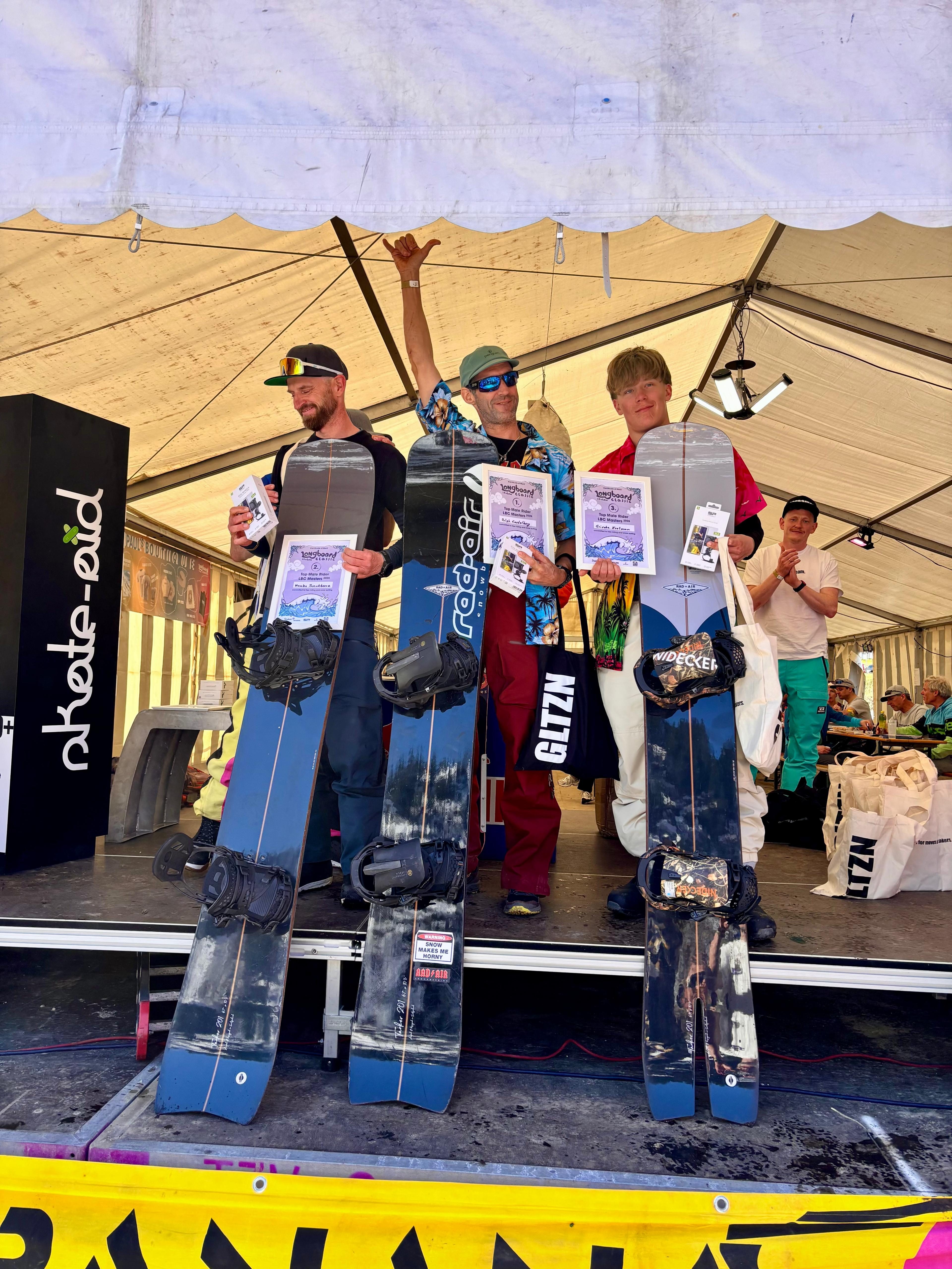 Siegerehrung – drei Herren auf der Bühne mit dunklen Boards, Skate Aid Banner